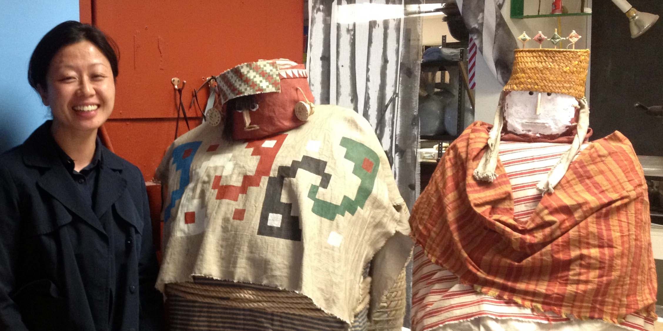 A woman standing next to two human-like figures draped in colorful cloth