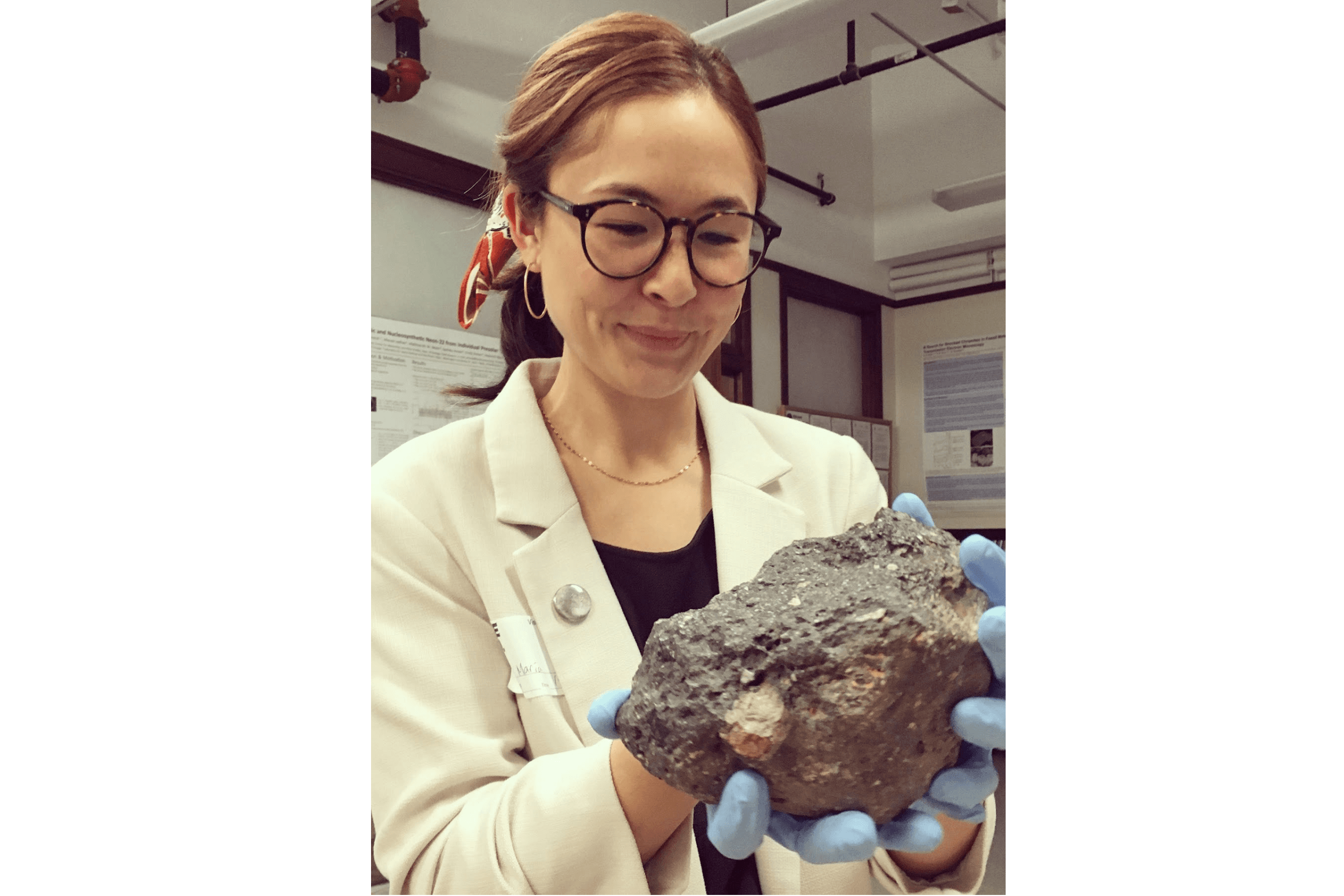 A woman stands holding a large rock in her gloved hands.
