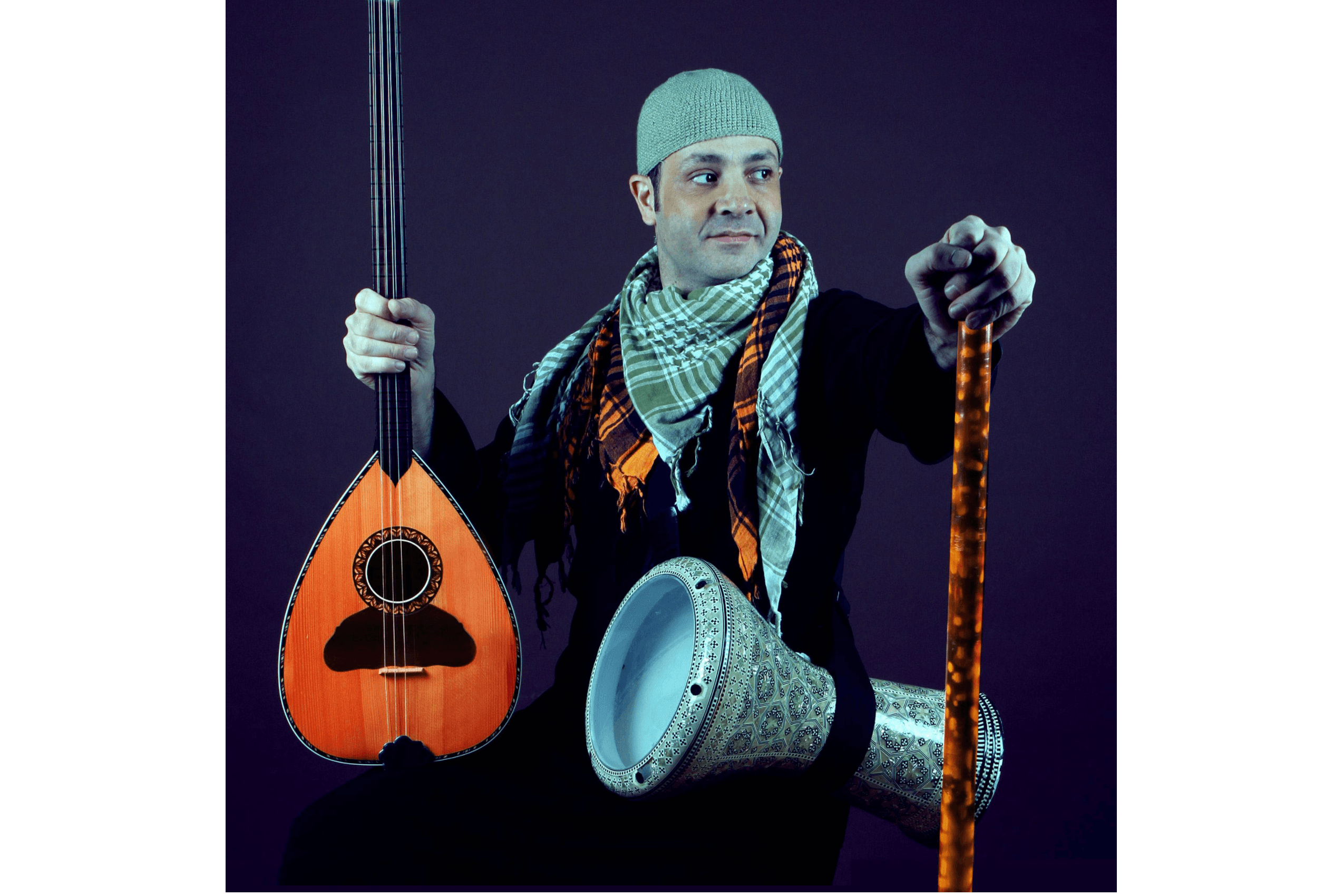 A man stands holding a string instrument in one hand, with another instrument over his shoulder.