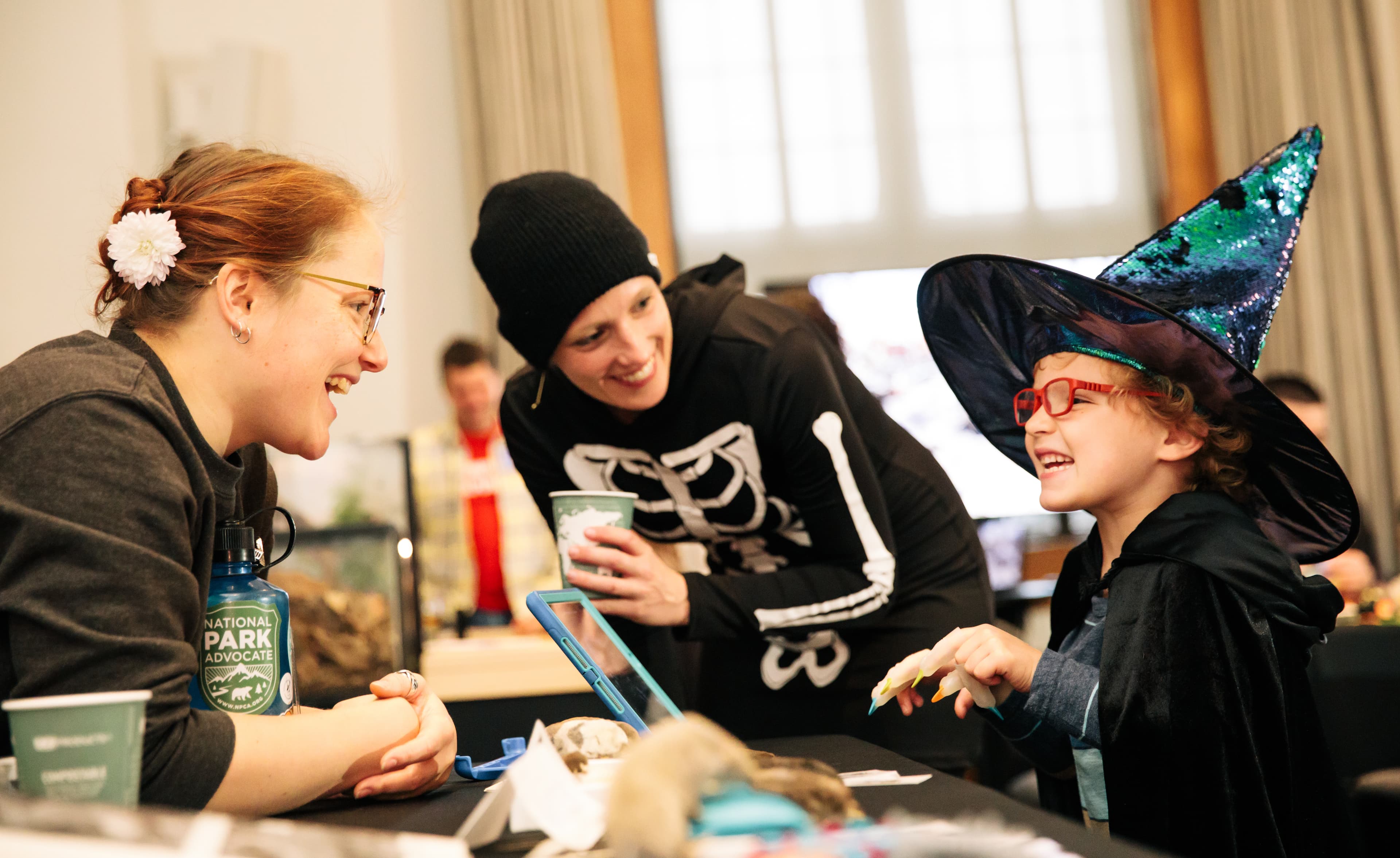 Two women and a girl, dressed for Halloween, talk around a table