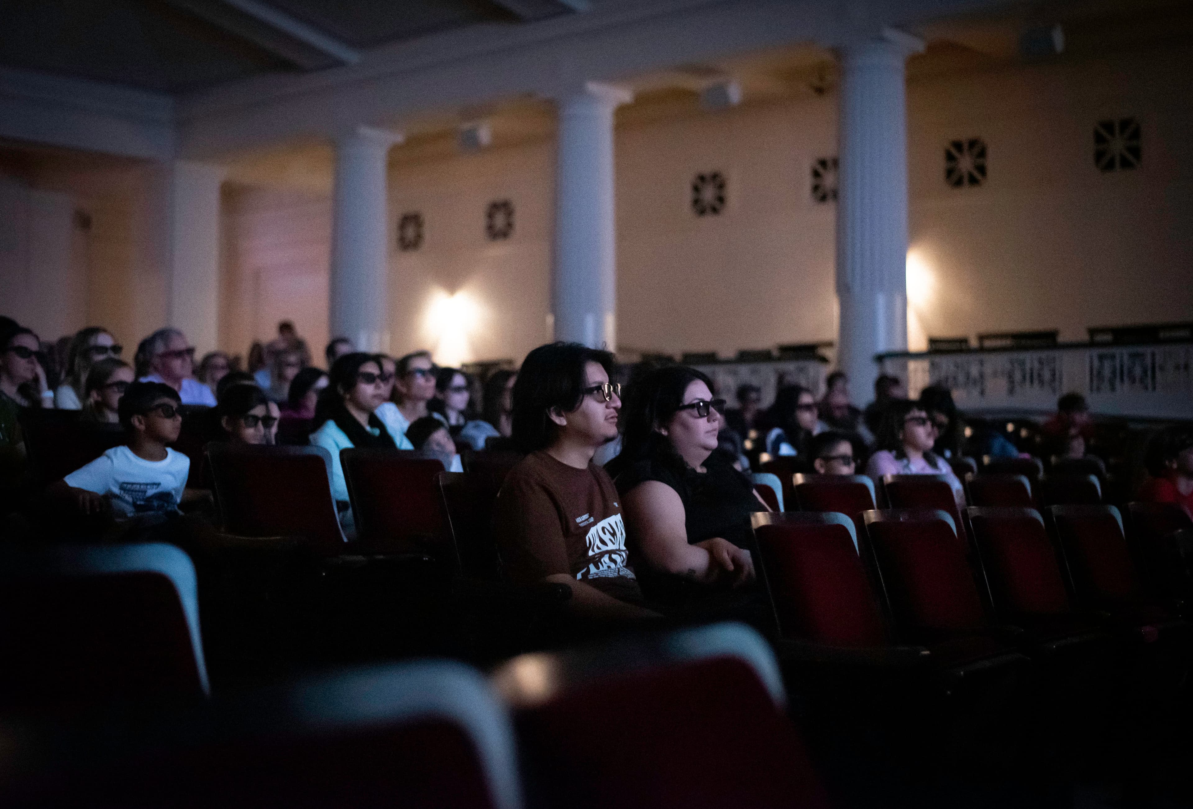 Visitors wearing 3D glasses seated in a theater.