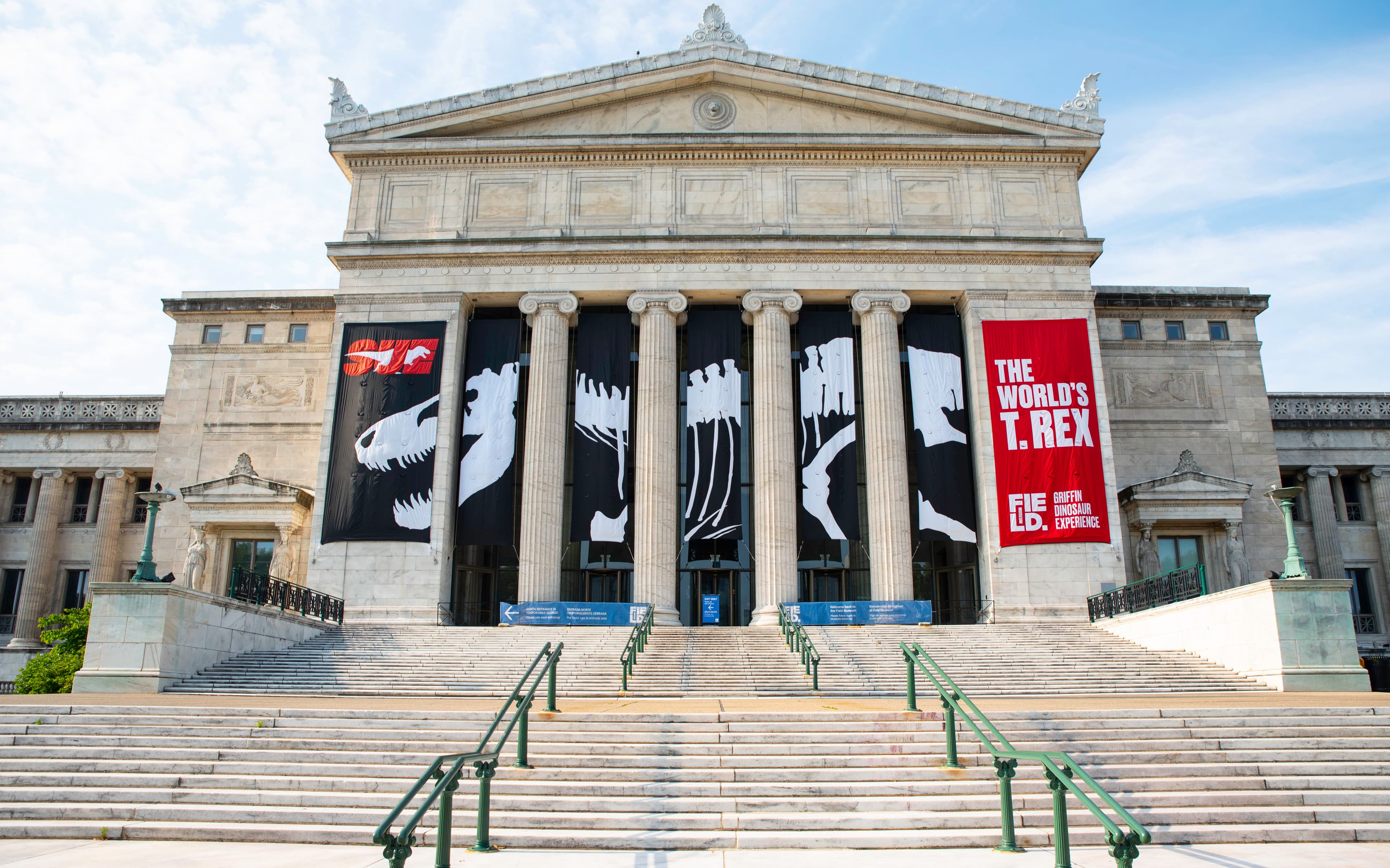 A large, classical building, with steps leading up to four ionic columns. Black, white and red banners are displayed on the building.