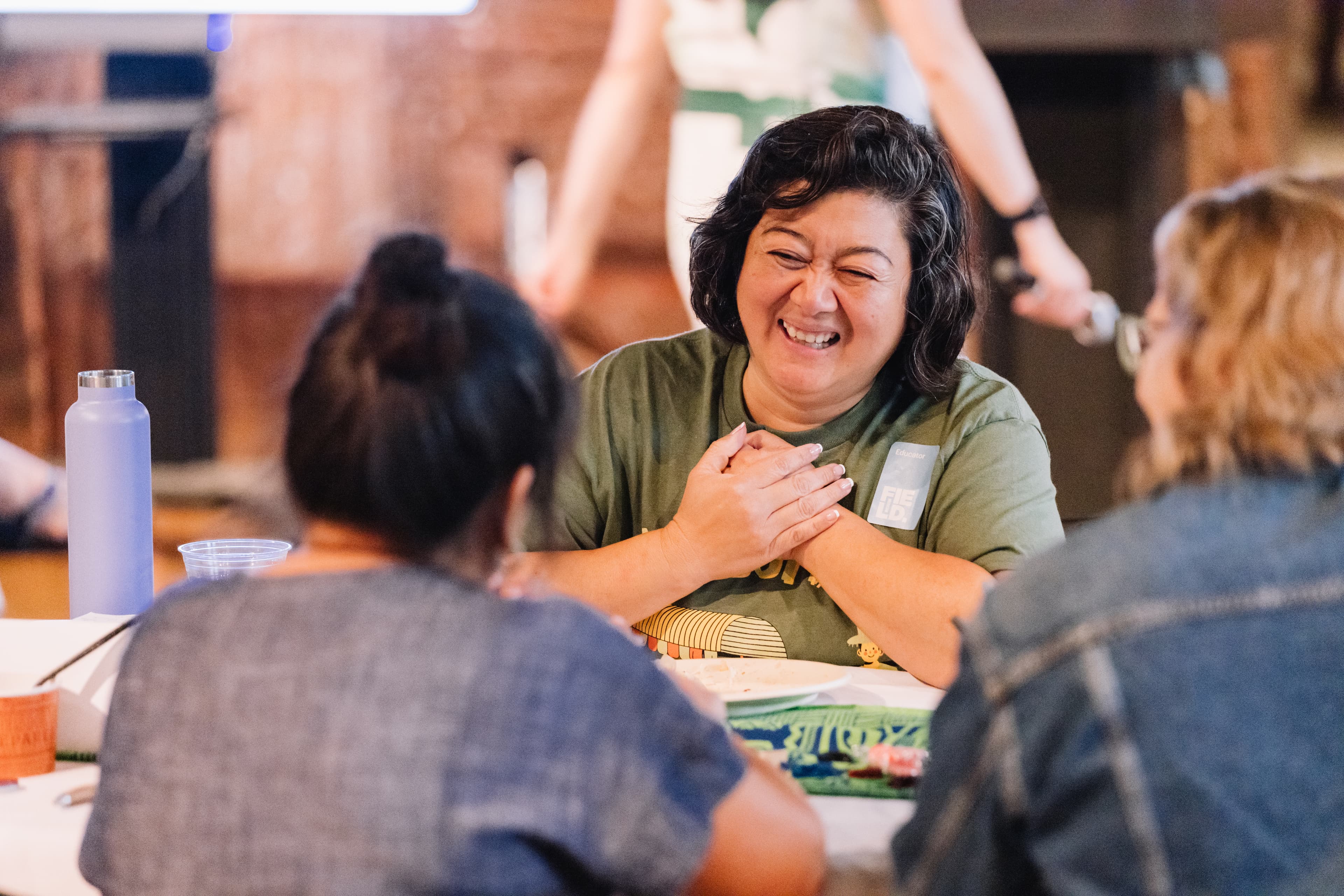 A woman holds her hands to her chest as she smiles at two other women she is seated across from.