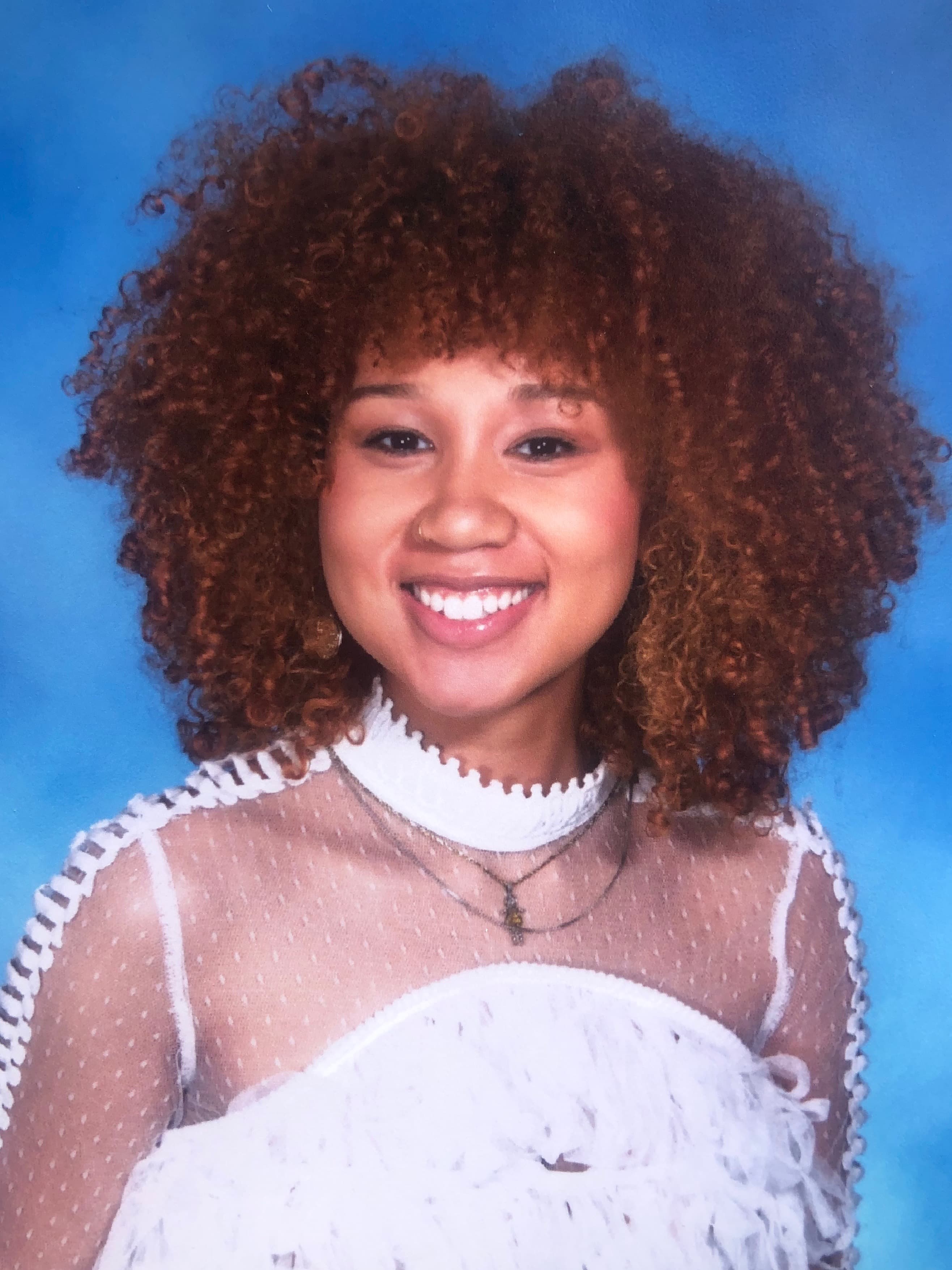 A woman with brown curly hair, wearing a white high-neck top.