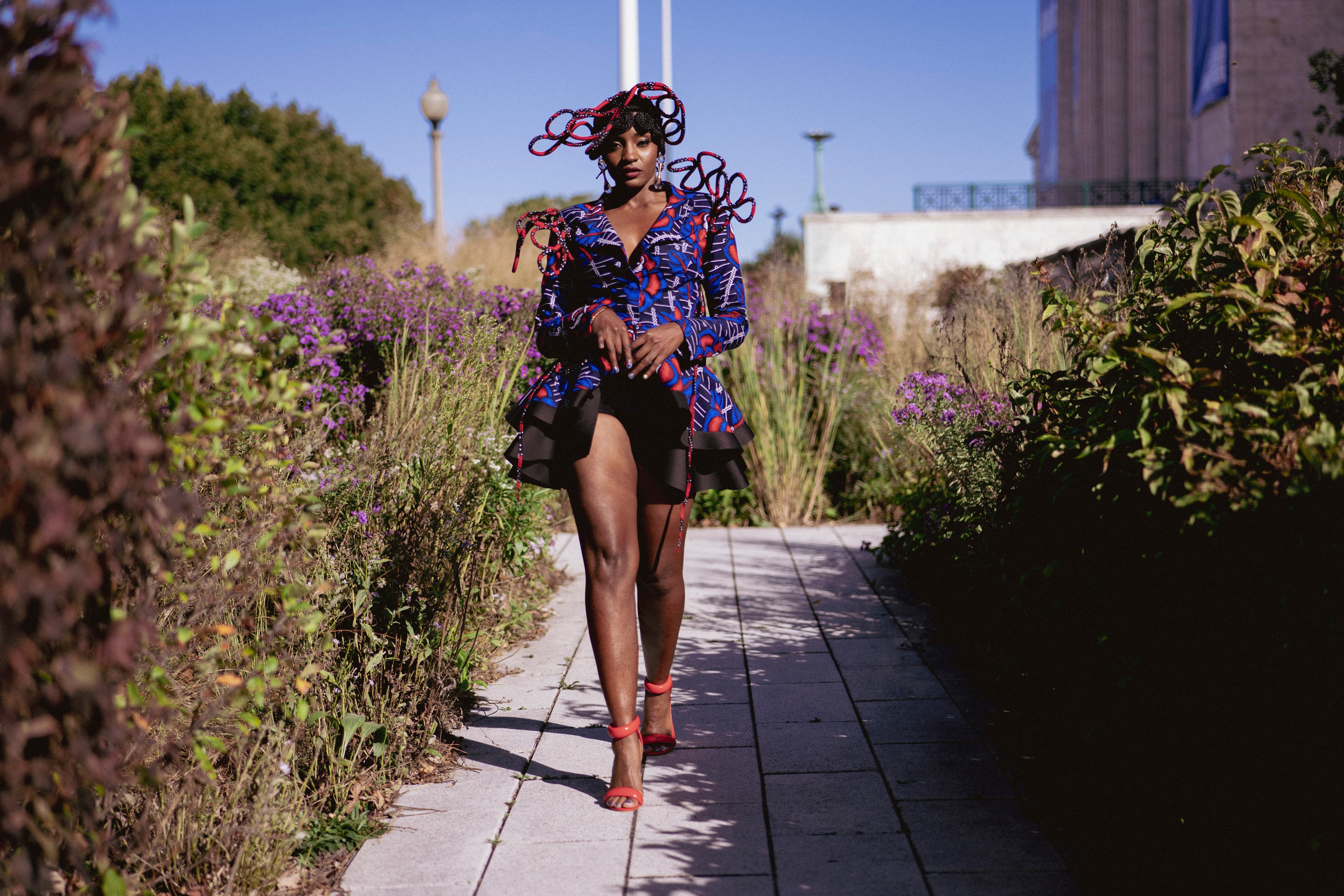 A model walks on a paver path through a garden with tall plants.