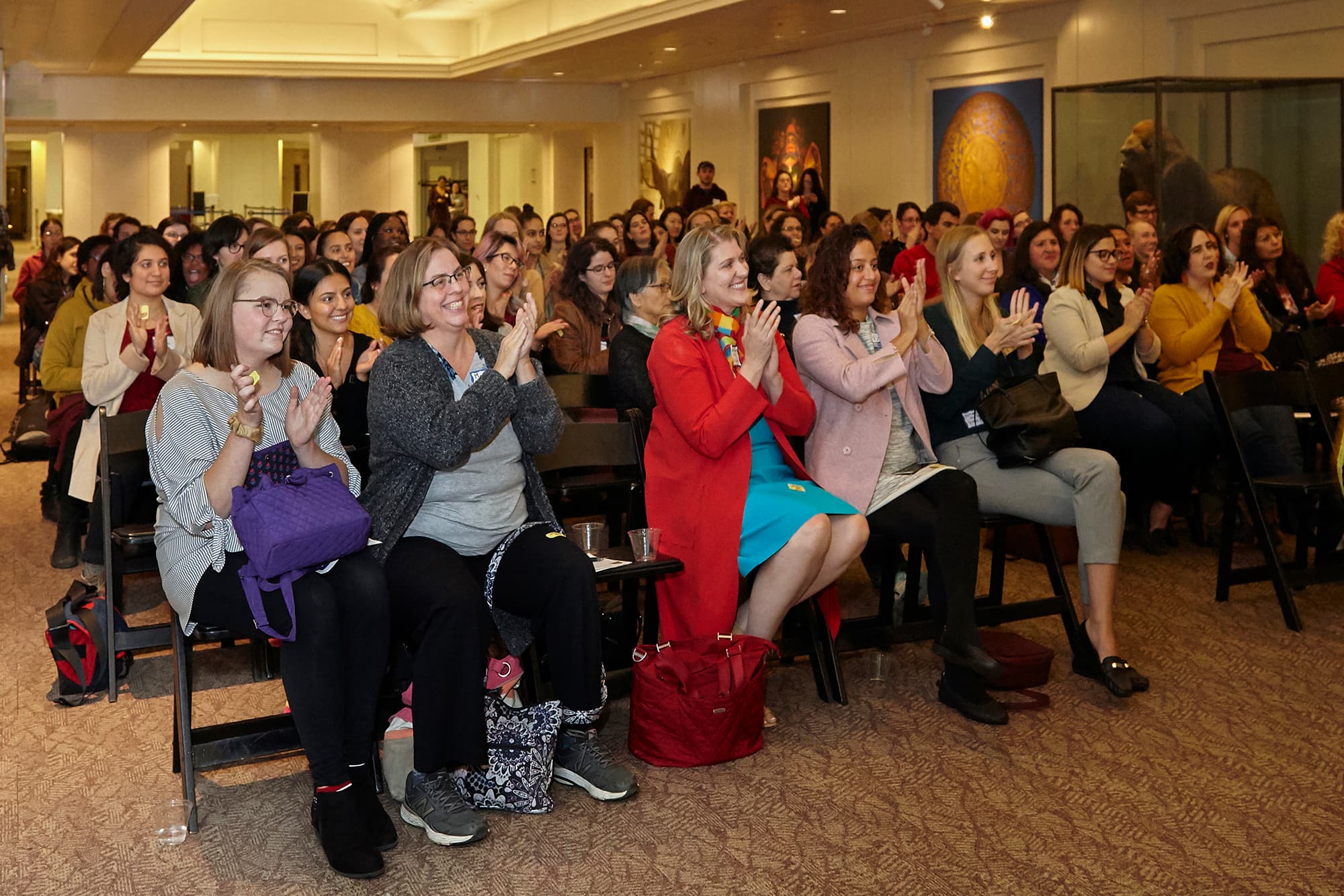 Women seated in rows of chairs, clapping.