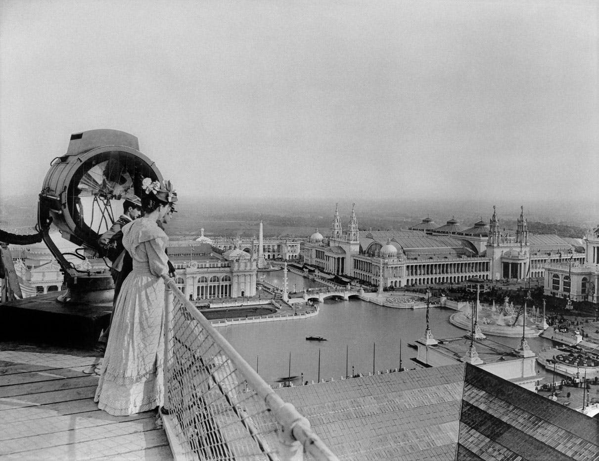 Two men and a woman stand on a roof, overlooking the World's Columbian Exposition, Chicago, 1893.