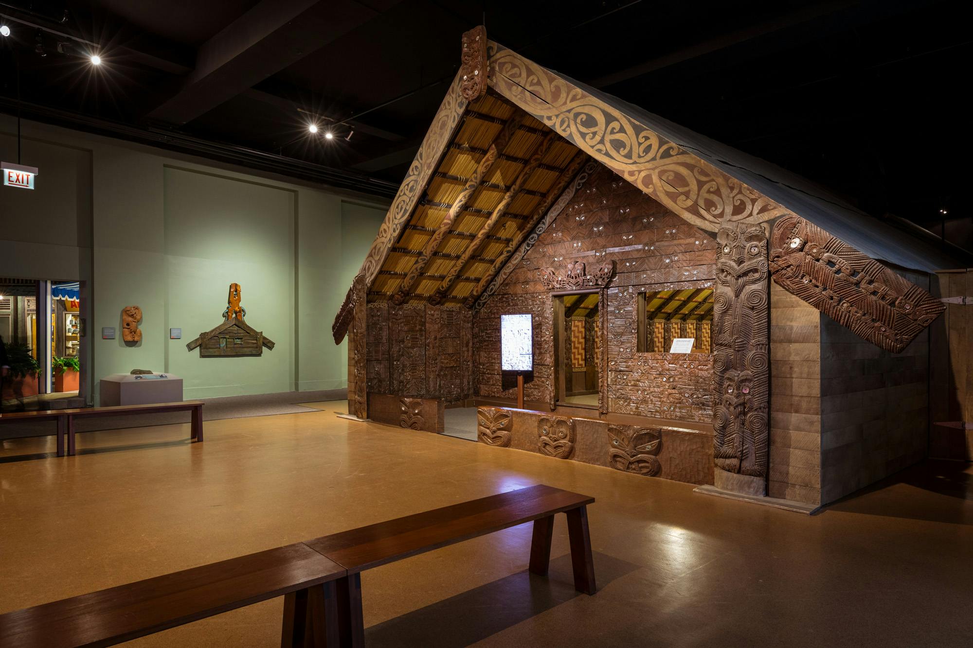 A three-quarter view of the front of the Maori Meeting HouseCarvings decorate the house’s walls and beams. At the apex of the gabled roof are two carved faces. One is Ruatepupuke, for whom this house is named.