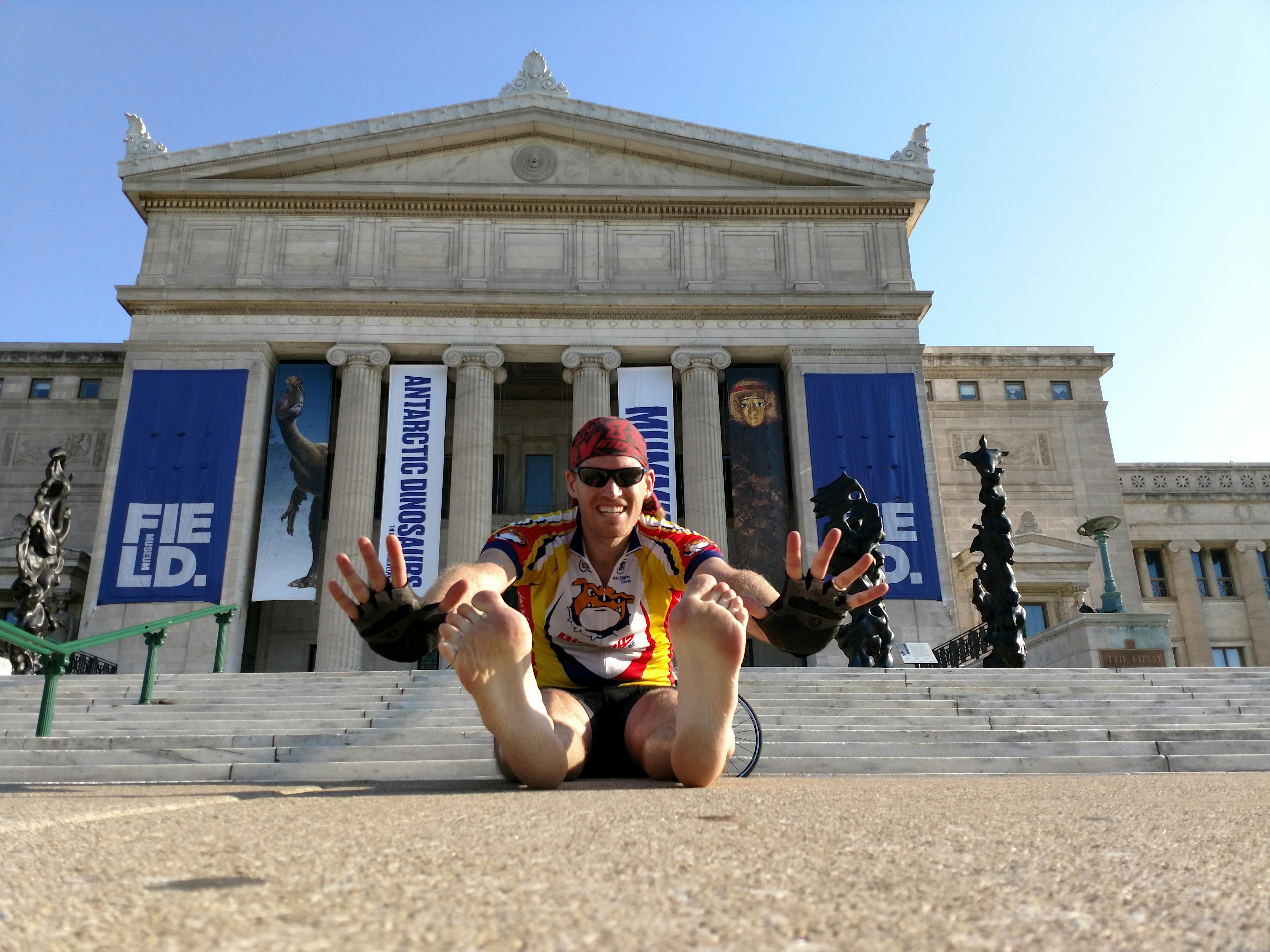 A man sits on the ground in front of the Field Museum's south steps.