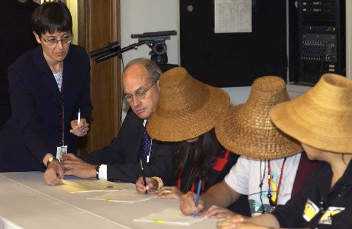 Four people signing documents, three of them wearing traditional Haida straw hats