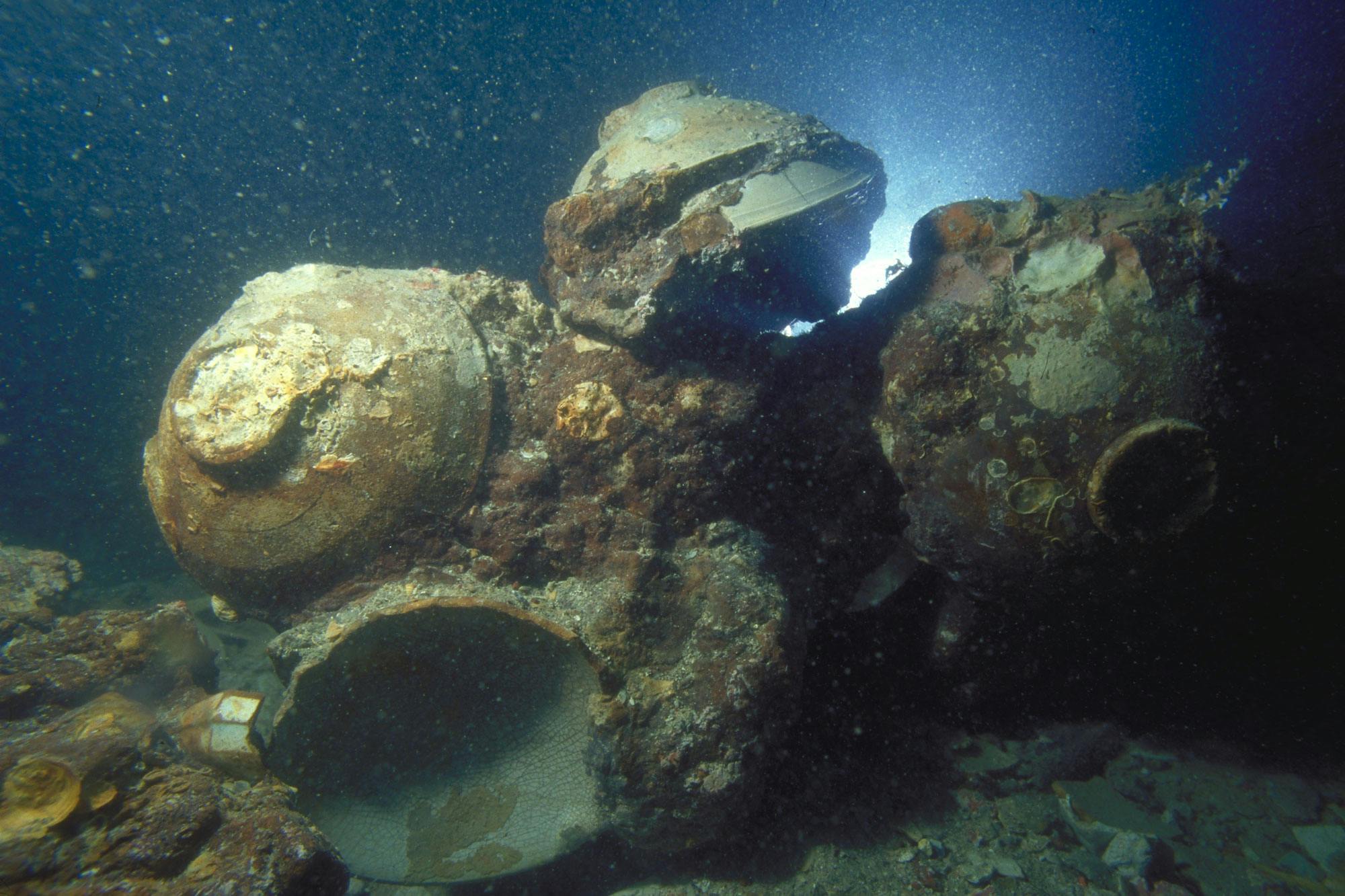 Several ceramic bowls rest on the seafloor, stuck together along with corroded iron and remnants of sea life.