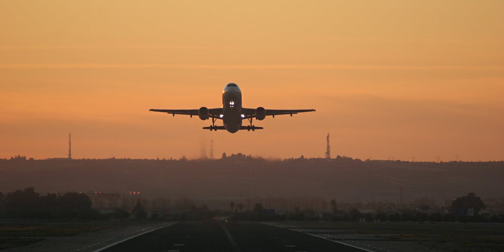 A plane taking off from a runway in front of an orange sky