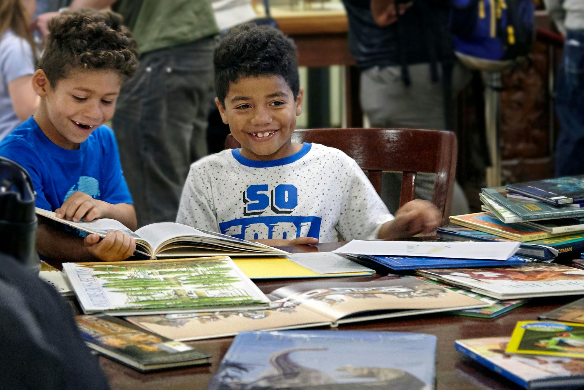 Two children seated at a table look at picture books.