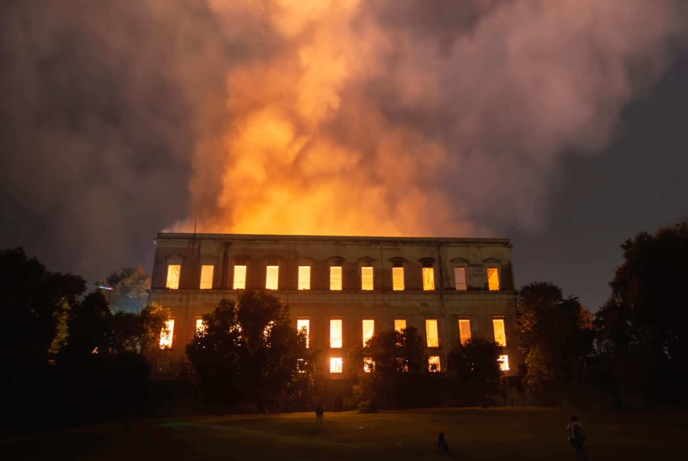 an building engulfed in flames, with orange-glowing smoke billowing up to the sky.