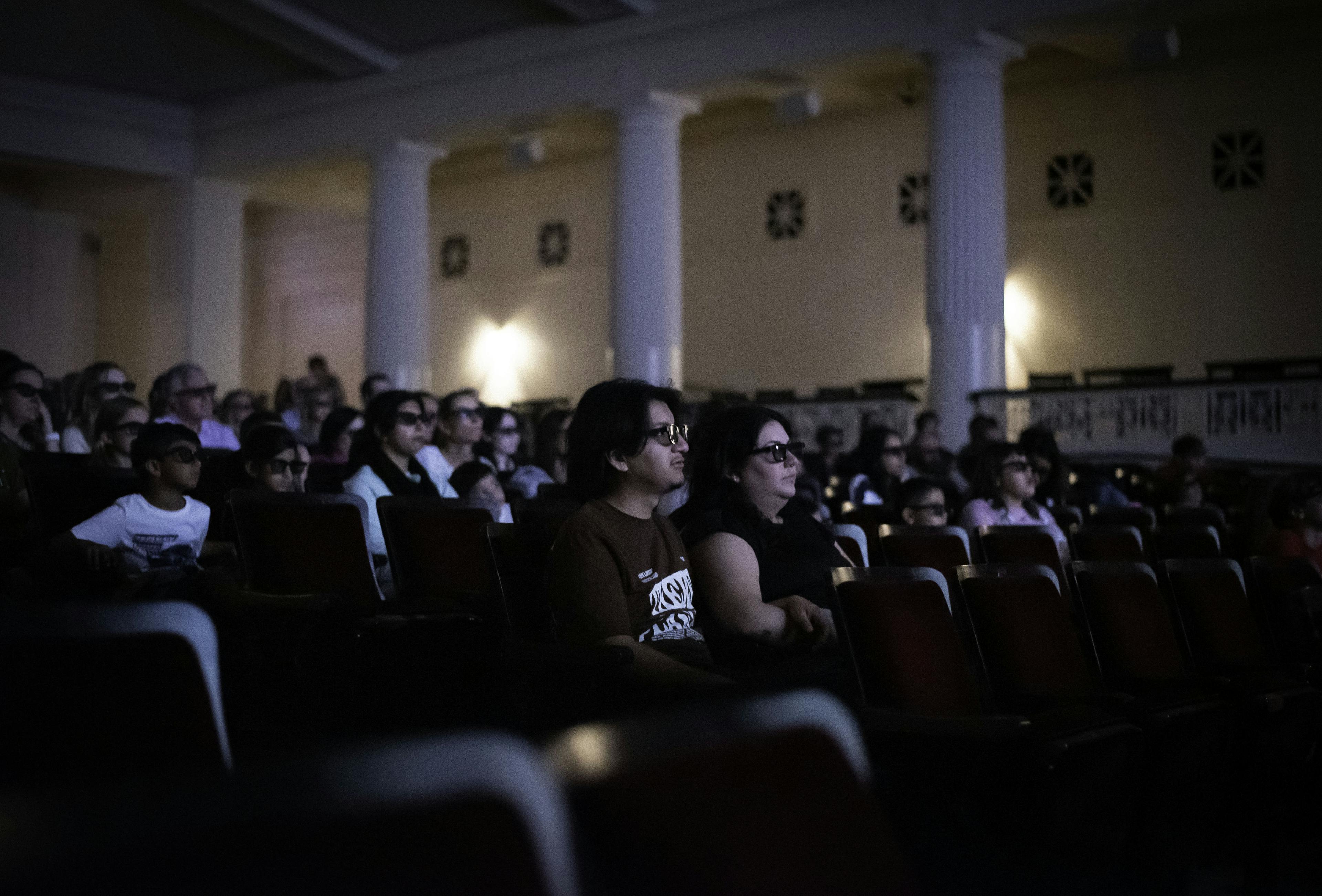 Visitors wearing 3D glasses seated in a theater.